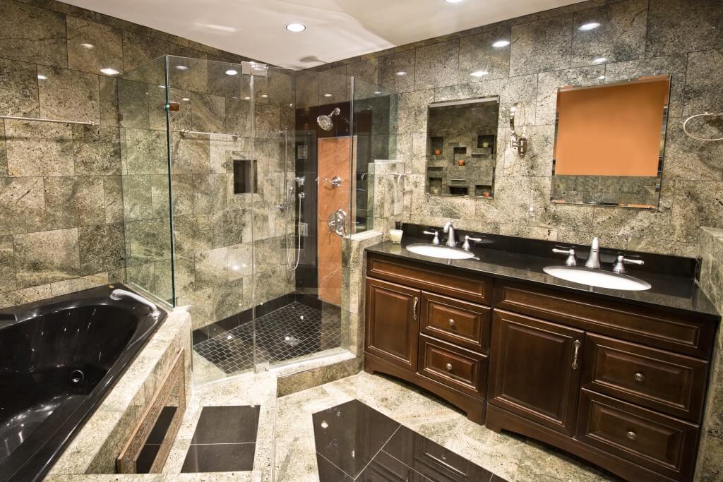 A dark, elegant bathroom with a wood vanity, black jetted tub, double wash basin, and walk-in shower with glass doors.