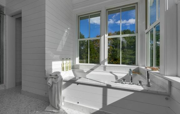 A white bathtub in a modern farmhouse bathroom with two double-hung windows above it