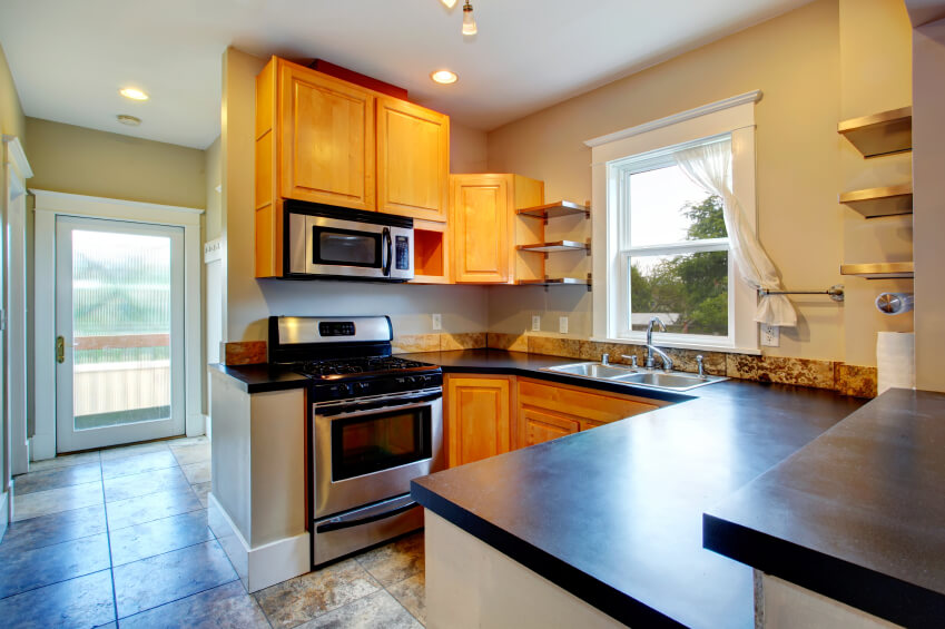 Modern kitchen with wood storage, black counter tops, steel appliances  and concrete floor
