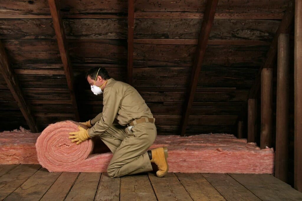 Contractor installing a roll of insulation in an attic space