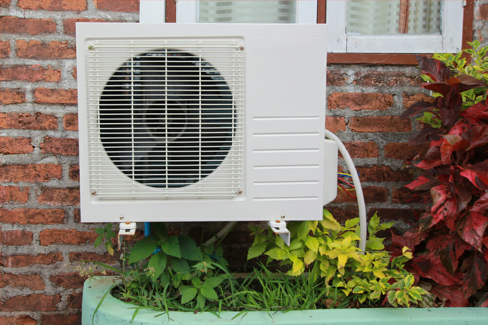 An external heat pump installed on a brick home on a spring day