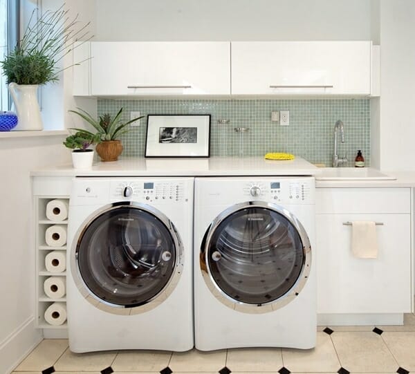 Image of a white laundry room with a green backsplash, a sink, and creative storage