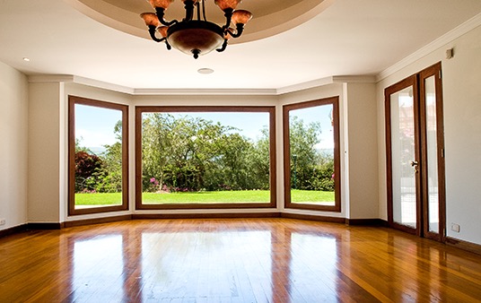 A wood floor in a living room leading to large picture windows.