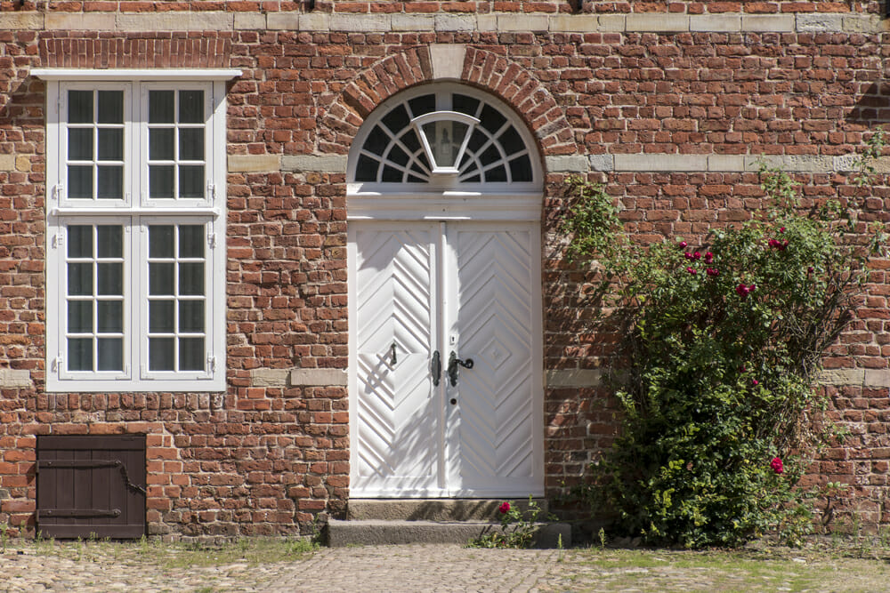 A white front door on a brick house with a half-moon window above it