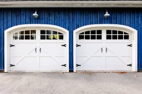 Two white side-hinged garage doors with windows on blue house