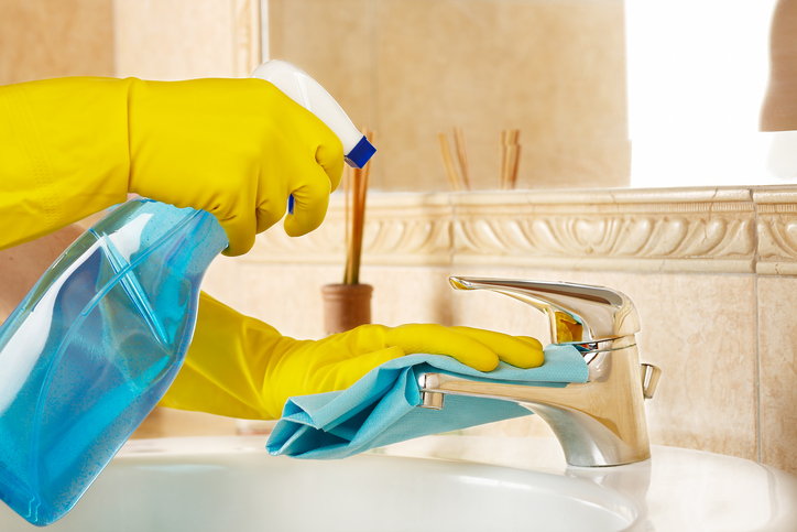 woman in rubber gloves with rag and detergent cleaning the bathroom