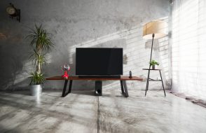 Modern living-room interior with TV in a loft style with wooden TV deck and concrete walls and floor . There are vintage fan and clock ,lamps and green plant to decorate .