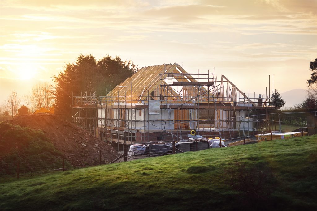 Image of an energy-efficient home being built in the framing stage with a sun setting in the back