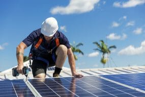 Solar panel technician with drill installing solar panels on roof on a sunny day