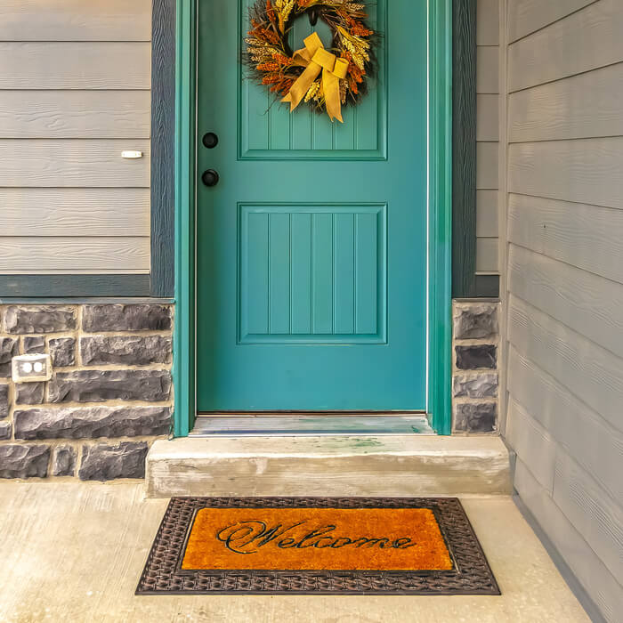 Welcome doormat in front of a door with wreath. A welcome doormat in front of the blue green door of a home. A festive wreath with golden bow is hanging on the lovely front door.