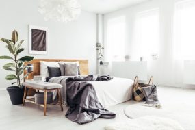 White spacious bedroom interior with windows, potted plant and basket with blanket standing by the bed