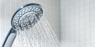 Modern blue shower head with running water in white bathroom.