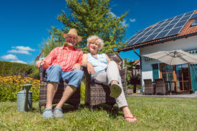 Low-angle view portrait of a happy senior couple in love sitting on chairs while relaxing together in the garden at home in a sunny day of summer