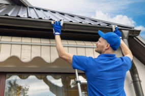 person installing gutter system onto metal roof