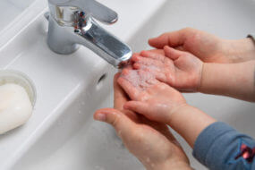 mother helping little child to wash hands over a white sink