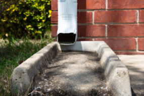 image of a white gutter downspout leading into a concrete water guide
