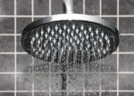 Closeup image of a chrome rain showerhead against a gray tile background