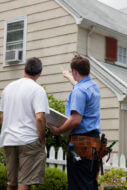Service contractor pointing to home exterior with homeowner, rear view