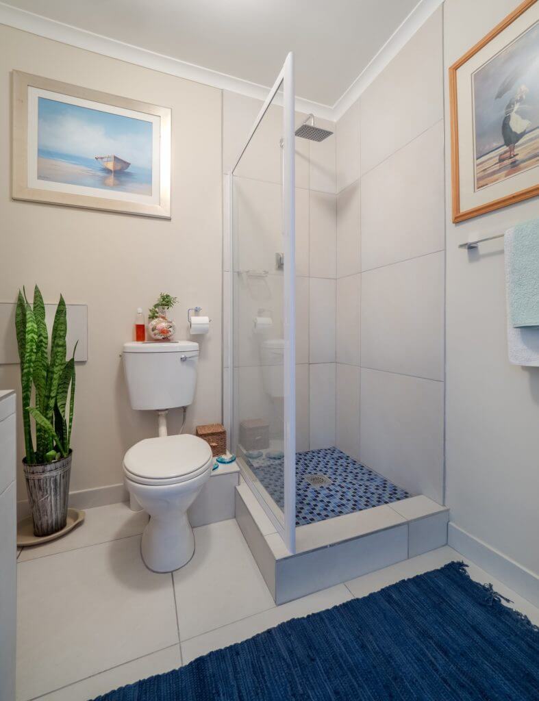 Small bathroom with corner shower with blue shower floor next to white floor