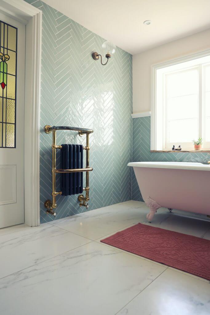 Large bathroom with clawfoot tub, herringbone tile on the walls, and stained glass door