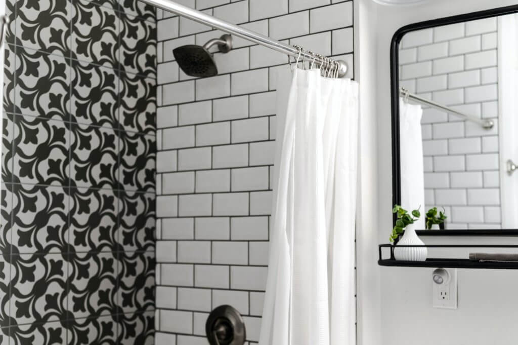 Black and white tile on shower wall next to white subway tile with dark grout