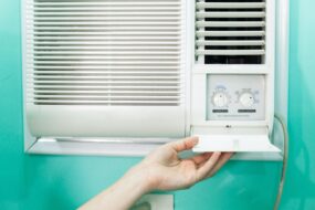 Image shows an in-wall ac unit against a green wall with a hand adjusting the knobs 