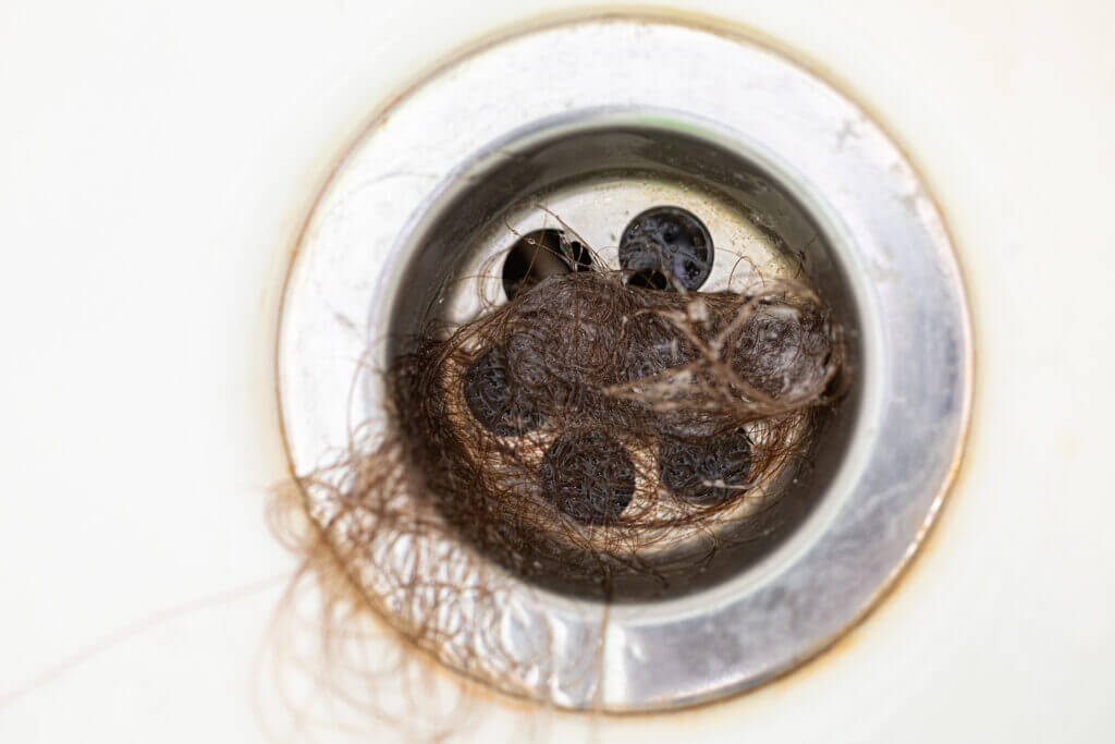 Close-up. Bathroom drain is clogged with dark human hair. Means for cleaning pipes and plumbing. Cleaning bathroom. Sanitation and hygiene. Stress and illness. Alopecia. Metabolic disorders.