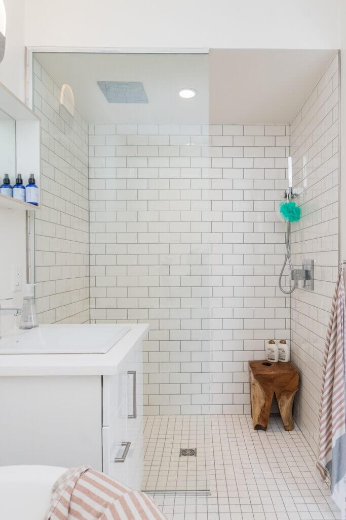 Image shows a white subway tile shower with glass front and recessed lighting