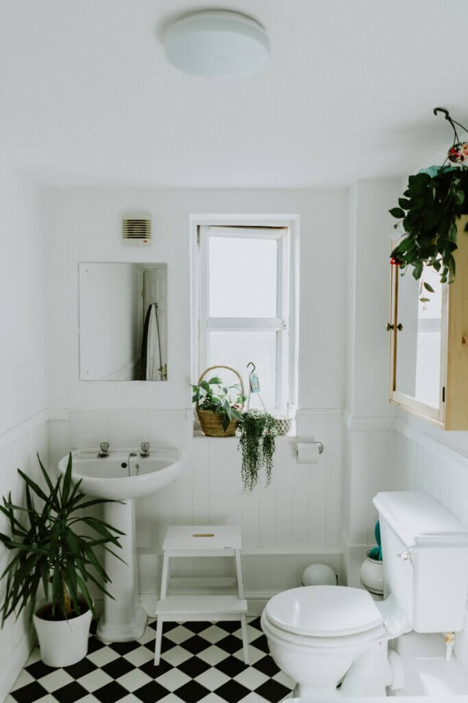 Half bathroom with black and white tile floor, white toilet and sink, and lots of greenery.