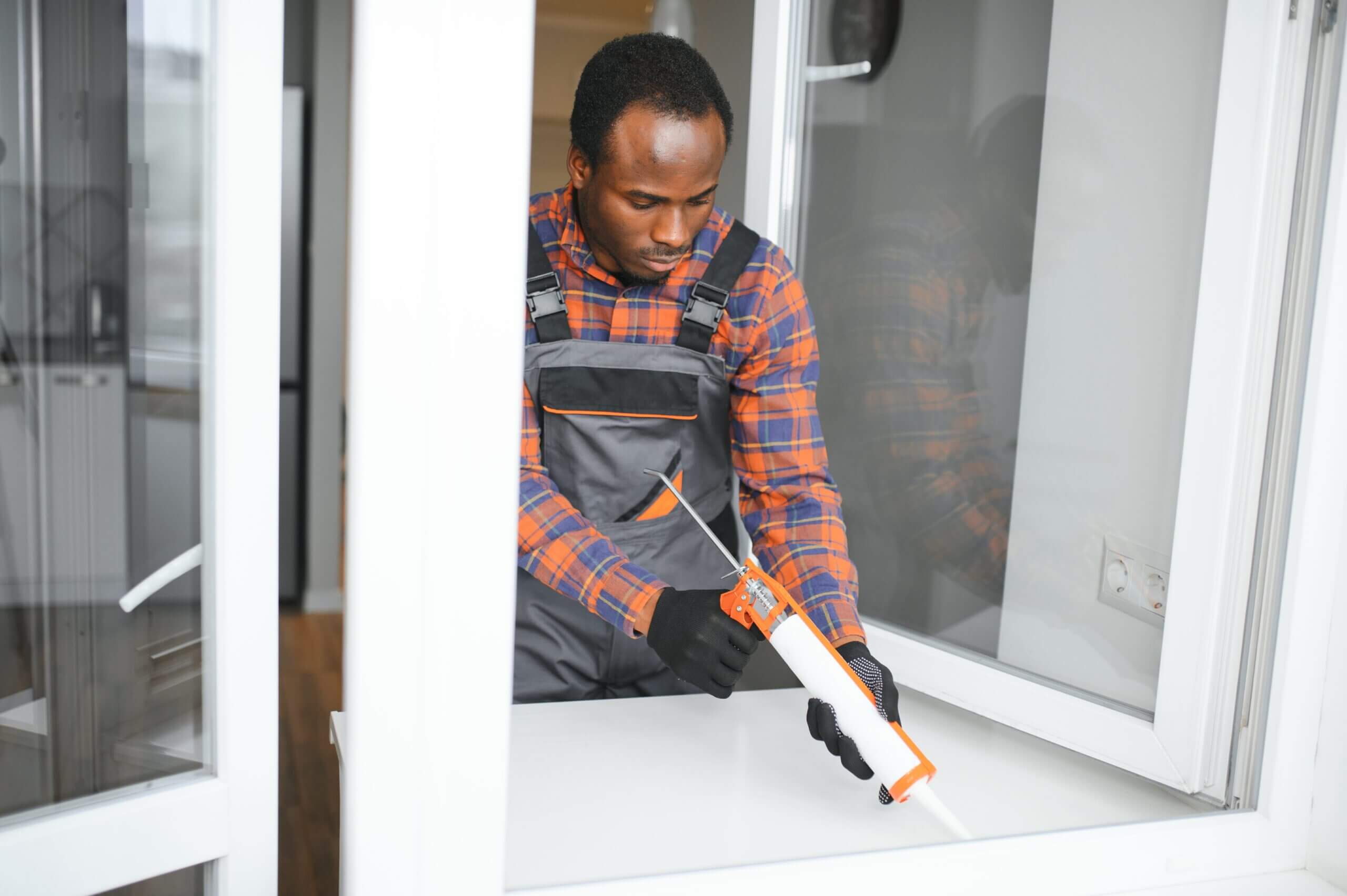 A window installer apply window sealant to the edge of an open window 