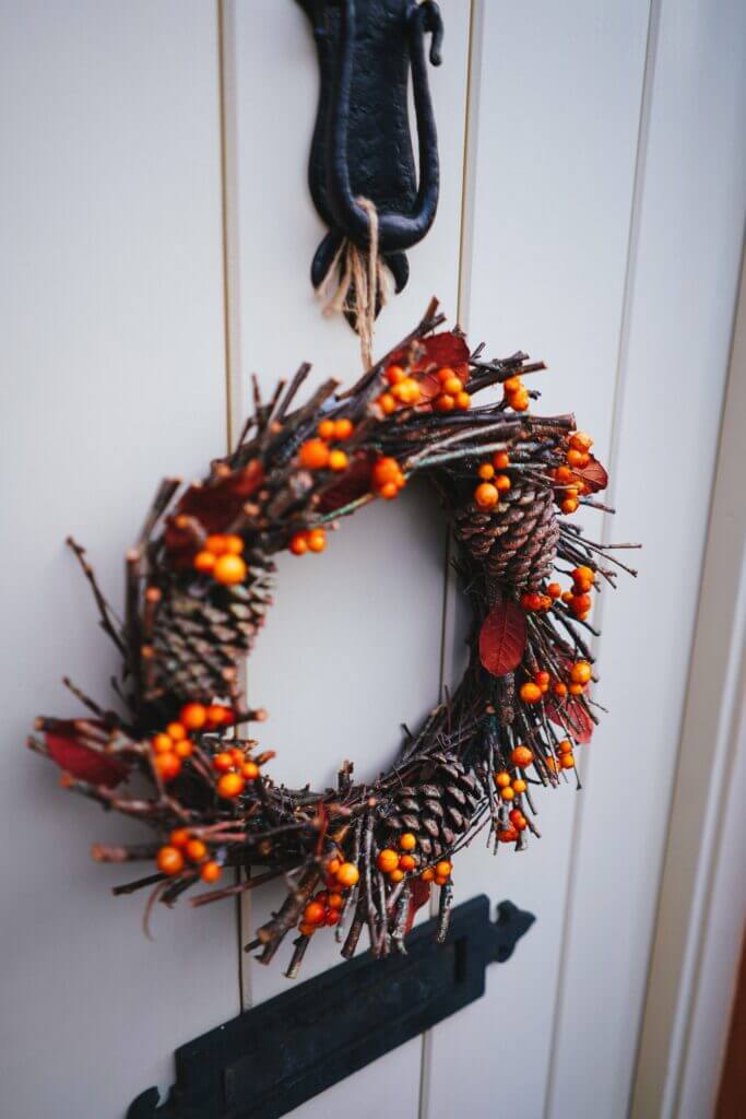 Close up image of a fall wreath with pumpkins, pinecones, and greenery