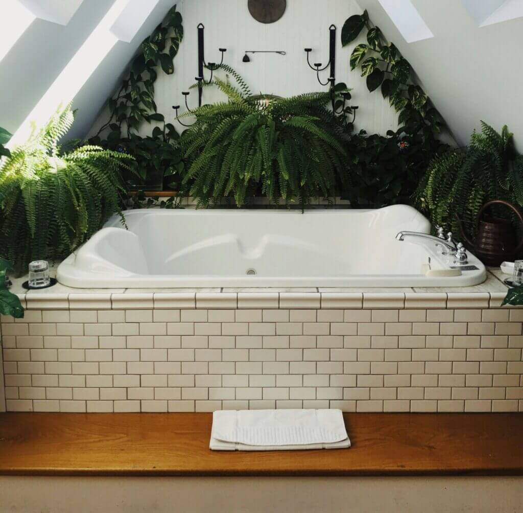 Drop in tub with white tile surround in a plant-filled bathroom with skylights
