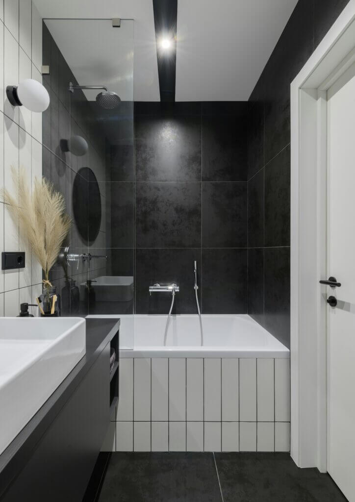 A modern bathroom with a tub and shower combo in vertical white tile and with a black tile surround