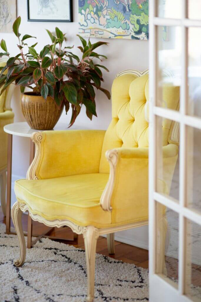 A bright yellow chair and plant at the entry of an open kitchen space with French doors