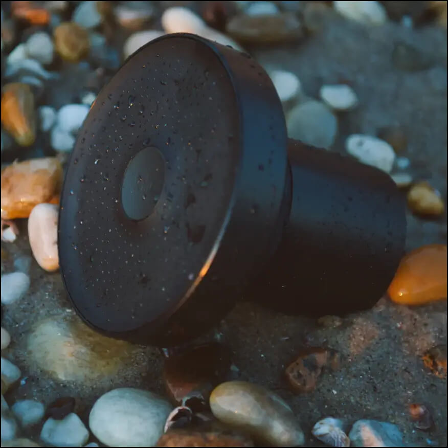 Close-up image of a black Jolie showerhead on a rocky riverbank.