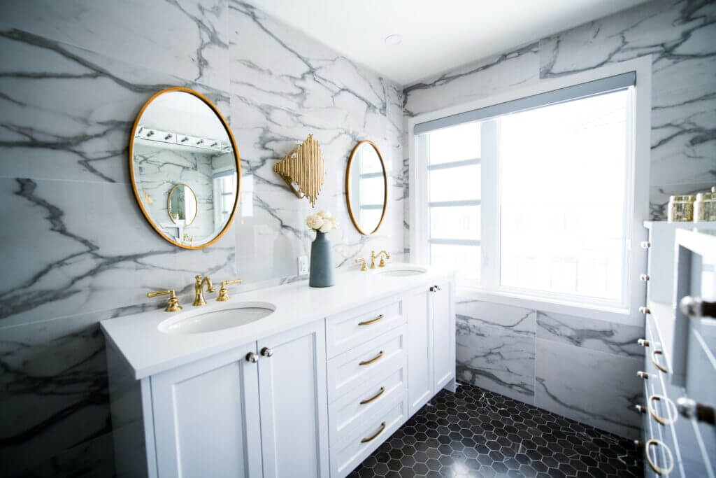 White vanities against white marble wall with gold mirrors