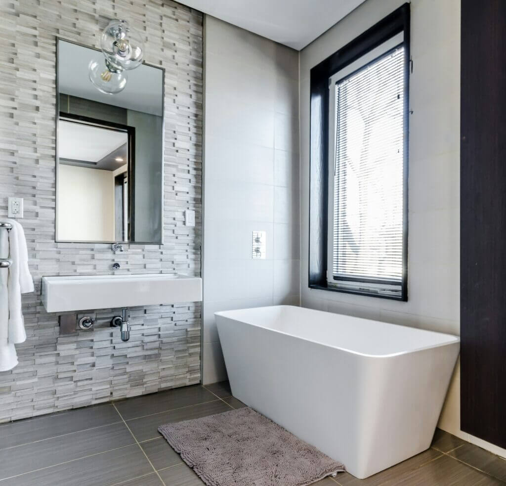 Freestanding tub in a white bathroom with a stone accent wall