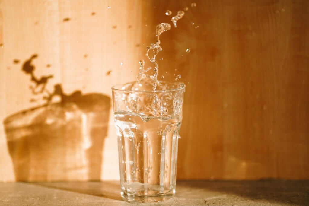 Water splashing out of a glass against an orange background in sunlight