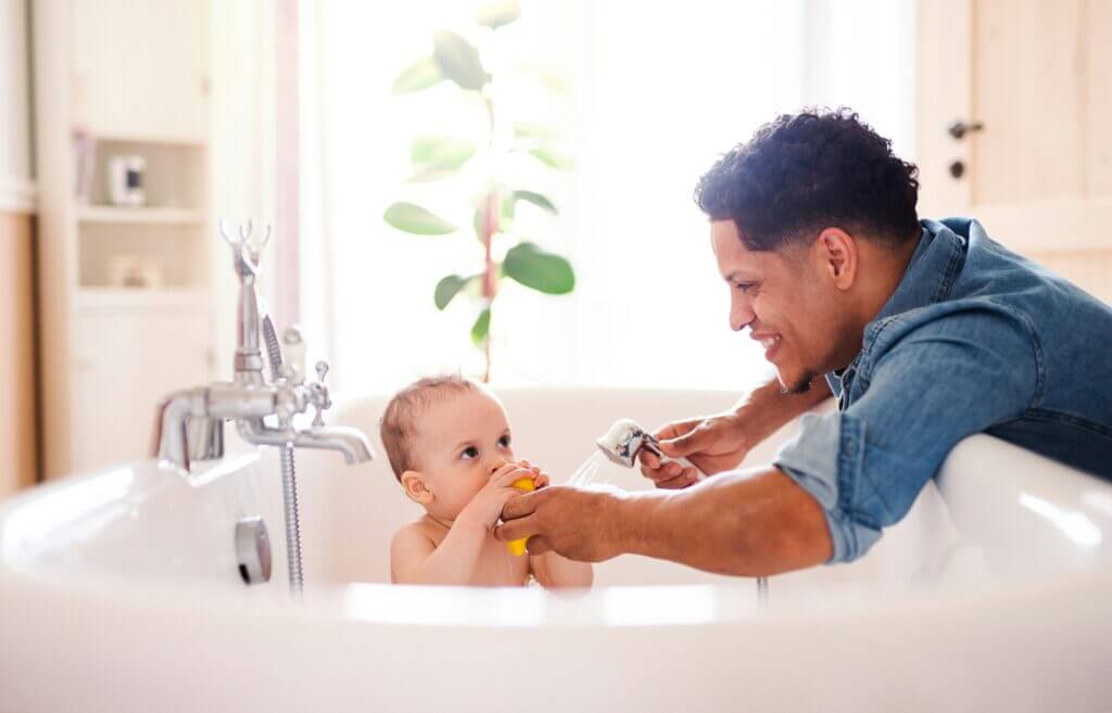 Parent bathing baby in bright, sunny bathtub