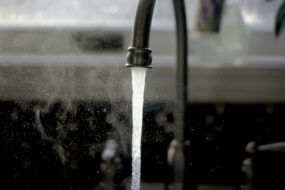 Black and white image showing a kitchen faucet on high