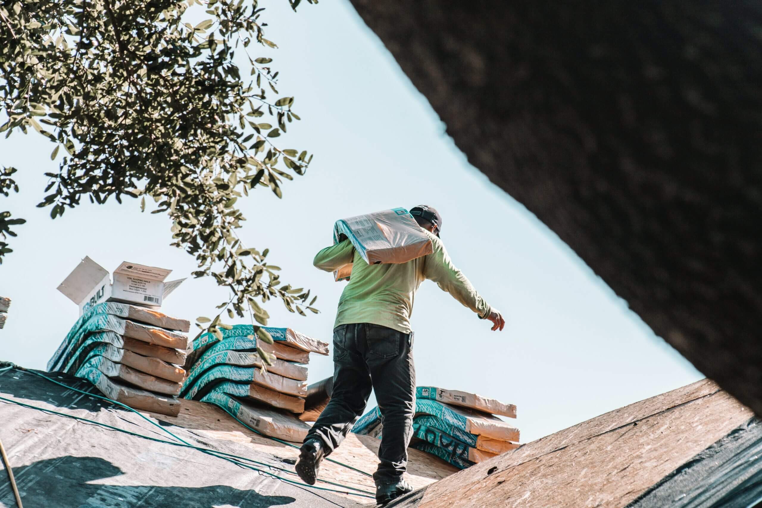 Construction worker carrying heavy shingles to be installed by the master roofer.