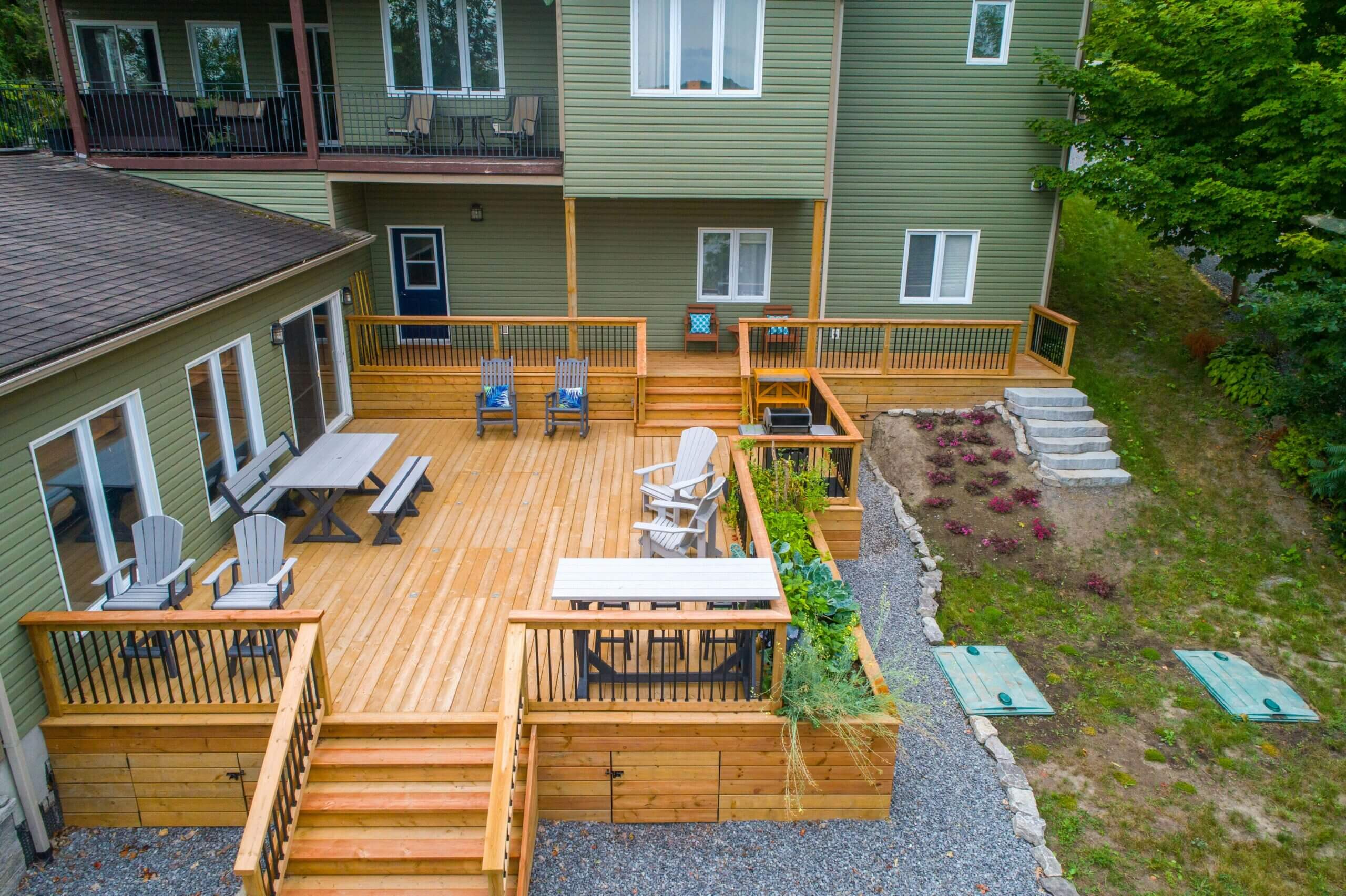 Large wooden deck attached to a green house with a railing and stairs
