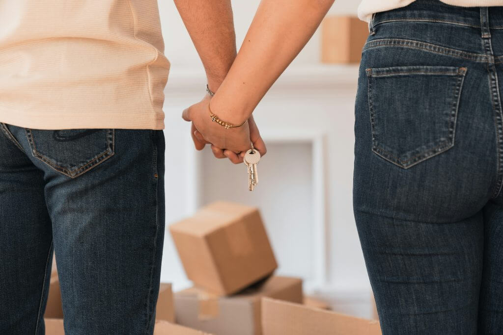 Image of couple holding hands with keys in a room with moving boxes