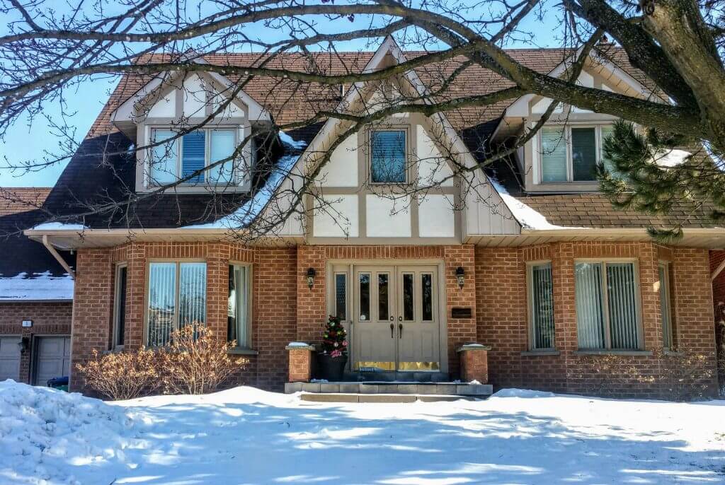 Photo of a brick home with snow on the roof and front yard
