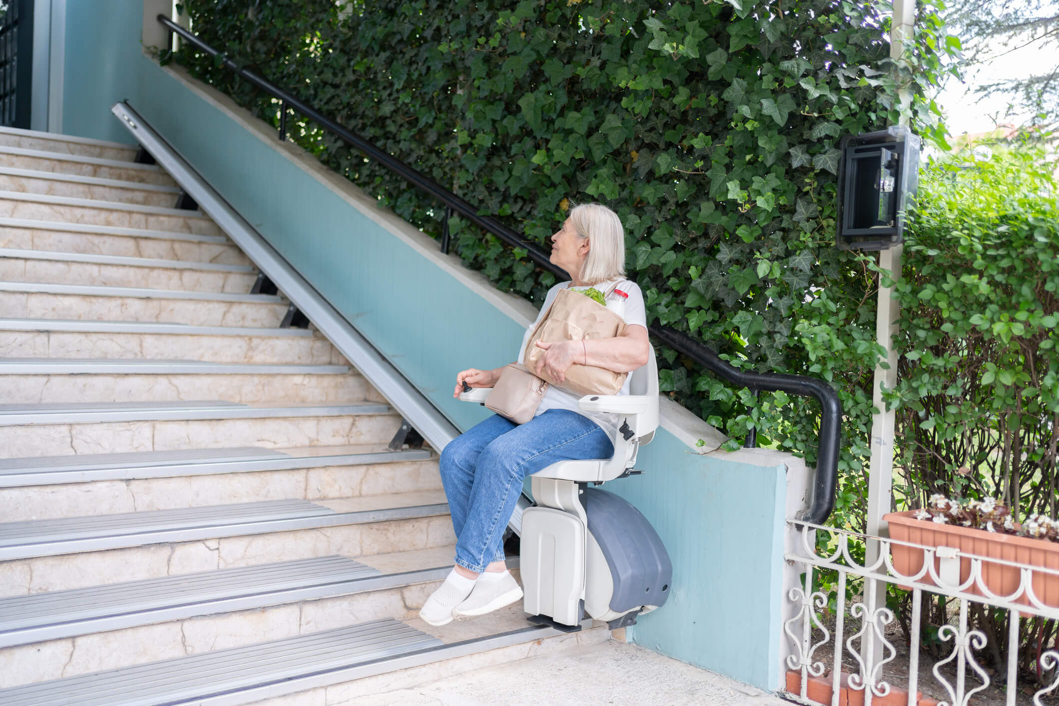 Senior Woman Using Automatic Stair Lift On A Staircase At The Apartment Entrance