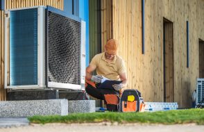HVAC technician working on a modern heat pump in front of a building.
