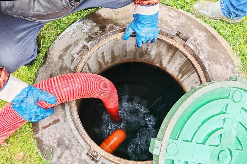 Service technician is using a hose to pump wastewater from a septic tank in a residential yard.