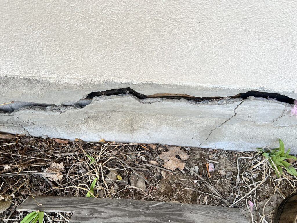 A wide crack runs through a house foundation.