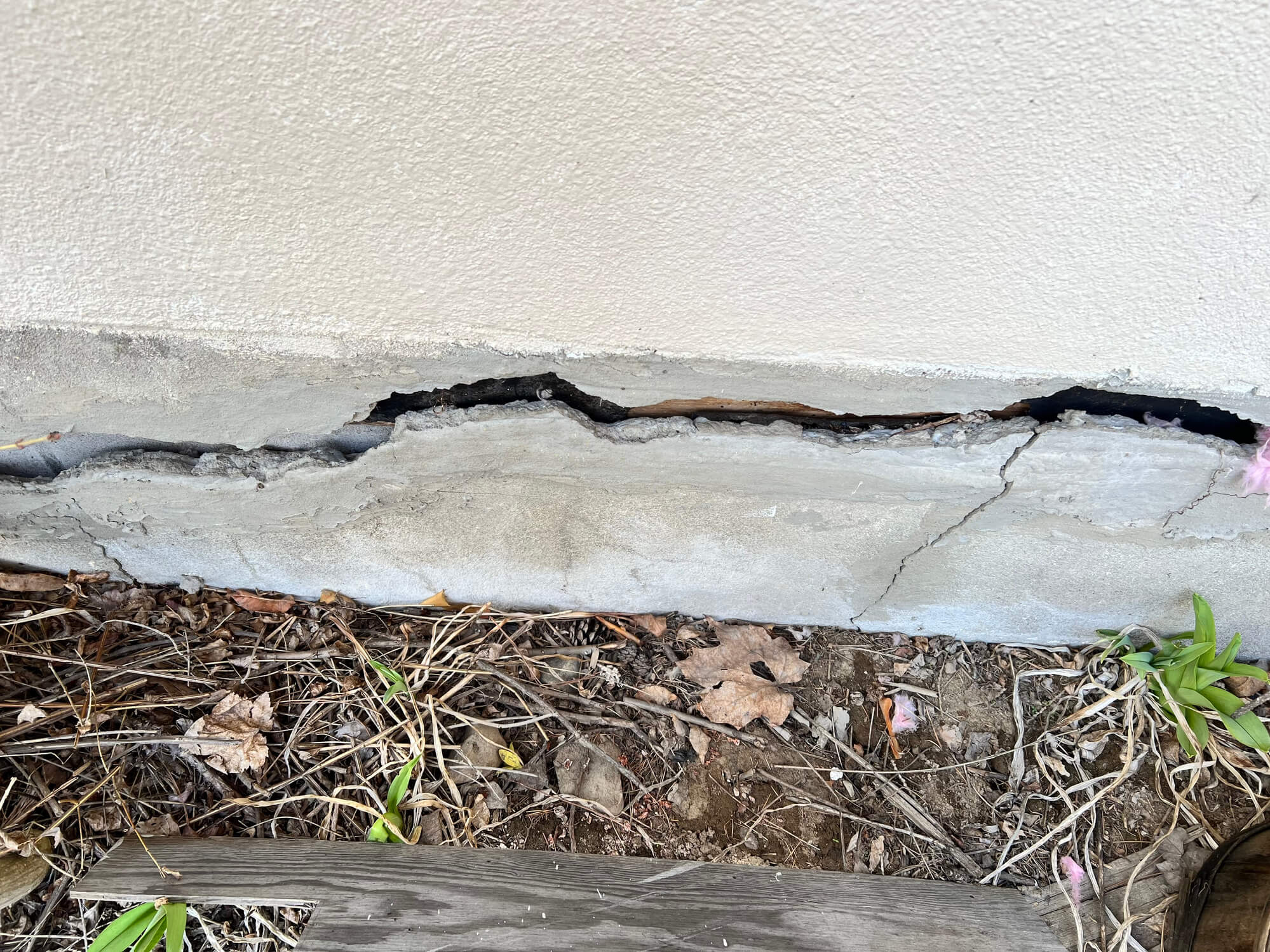 A wide crack runs through a house foundation.