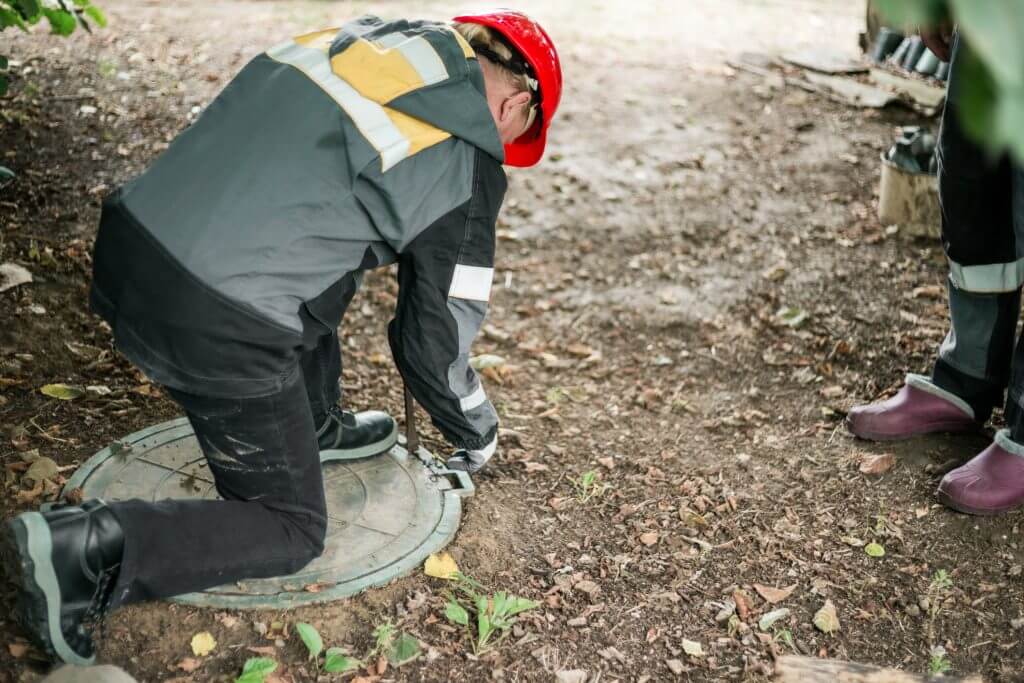 A worker leaned over a septic tank to open it for maintenance.